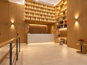 A reception area with a wooden reception desk, a seating area with a small table, and a wall with shelves containing books and decorative items. - Studio Apartment Adapted for People with Limited Mobility · Retiro (Madrid)