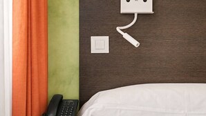 Une chambre d’hôtel équipée d’un lit, d’un téléphone sur la table de chevet, d’une prise électrique et d’une station de recharge fixée au mur.