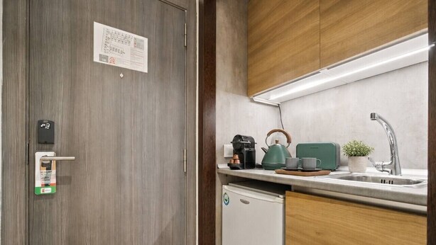 Une cuisine compacte équipée d’un lave-vaisselle encastré, d’une machine à café, d’une bouilloire et d’un grille-pain posés sur le plan de travail.