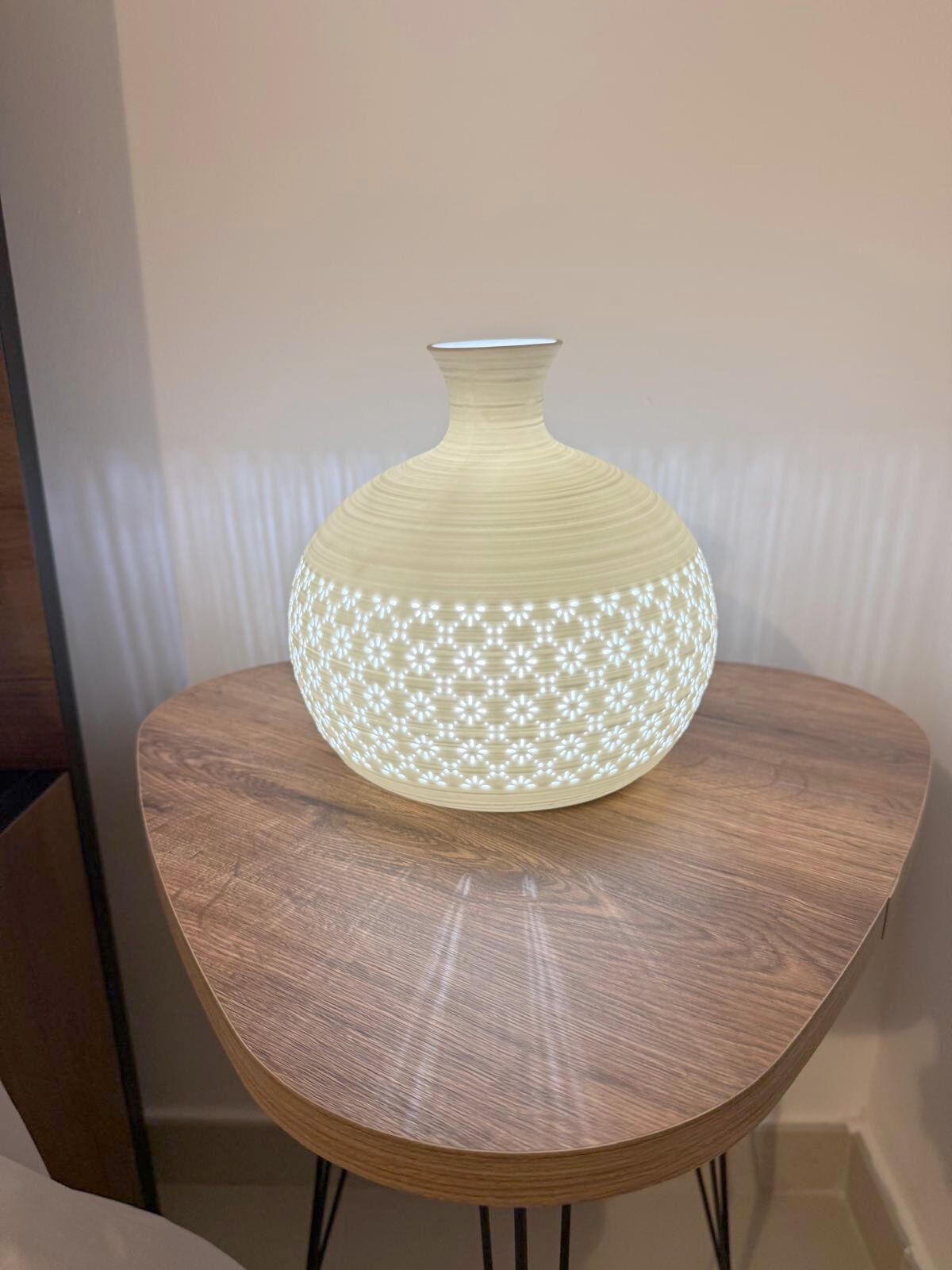 A round wooden table with a white vase on top.
