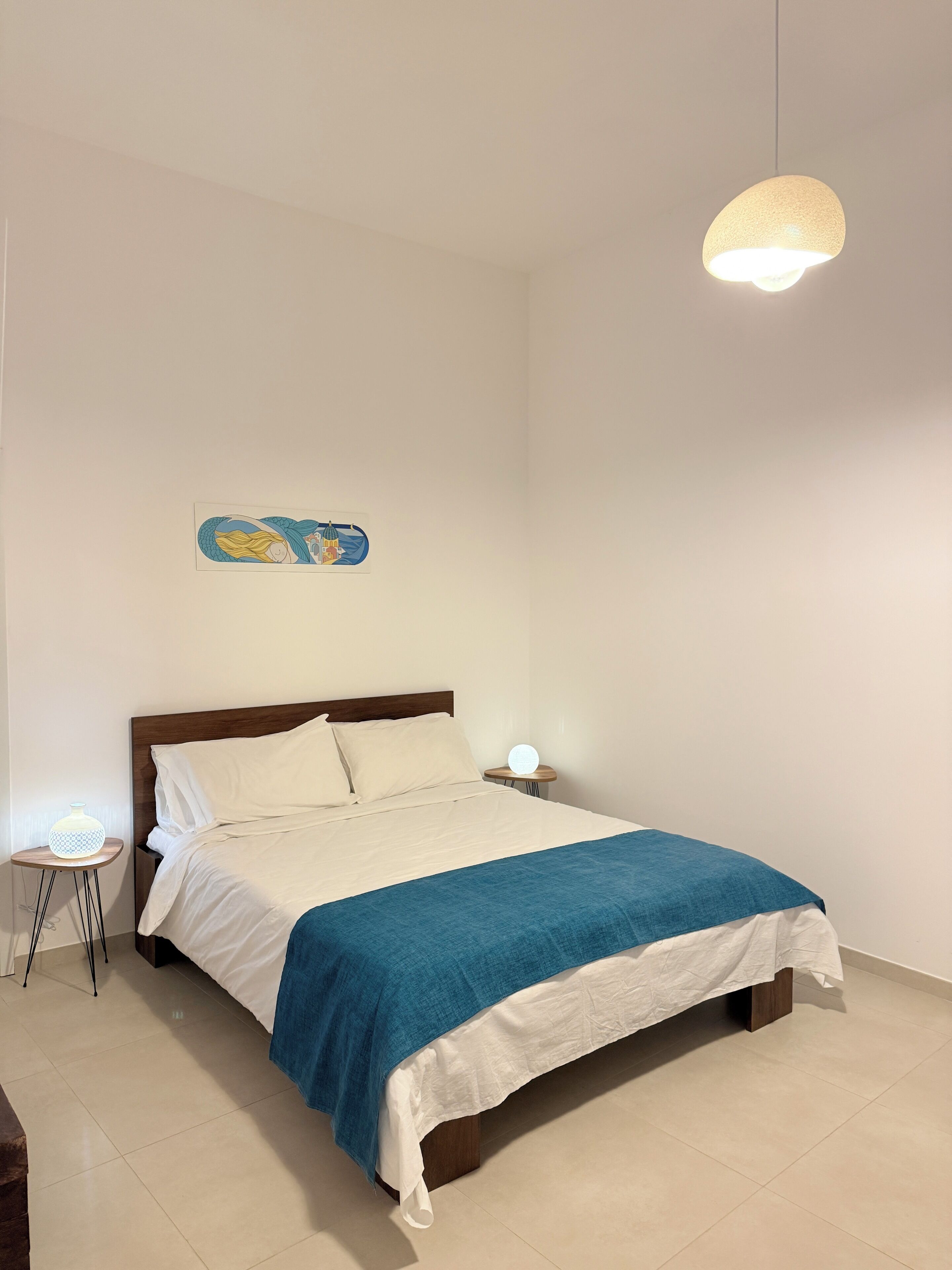 Un dormitorio con cama, mesitas de noche, una lámpara colgante y un adorno en la pared.