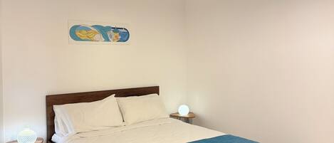 Un dormitorio con cama, mesitas de noche, una lámpara colgante y un adorno en la pared.