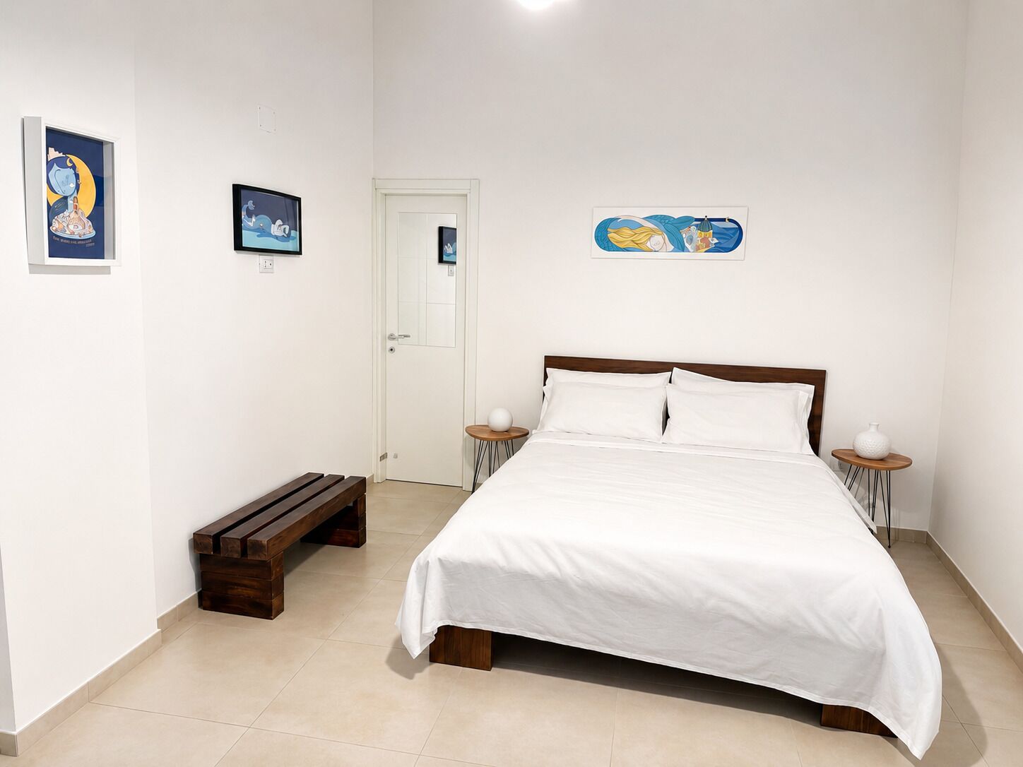 Ein Schlafzimmer mit einem Bett, zwei Nachttischen, einer Bank und Kunstwerken an den Wänden.