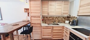 A compact kitchen with wooden cabinets, a dining table with chairs, and a coffee maker. - Charming apartment for 6 people with a mountain view (Les Deux Alpes)
