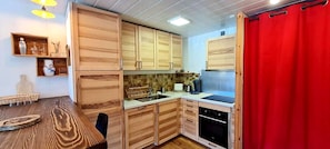 A compact kitchen with wooden cabinets, a sink, a stove, and a dining table. - Charming apartment for 6 people with a mountain view (Les Deux Alpes)