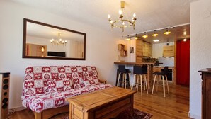 Una sala de estar con un sofá, una mesa de centro de madera, un televisor y una cocina al fondo.