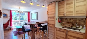 A kitchen with wooden cabinets, a bar stool seating area, and a window overlooking a balcony. - Charming apartment for 6 people with a mountain view (Les Deux Alpes)