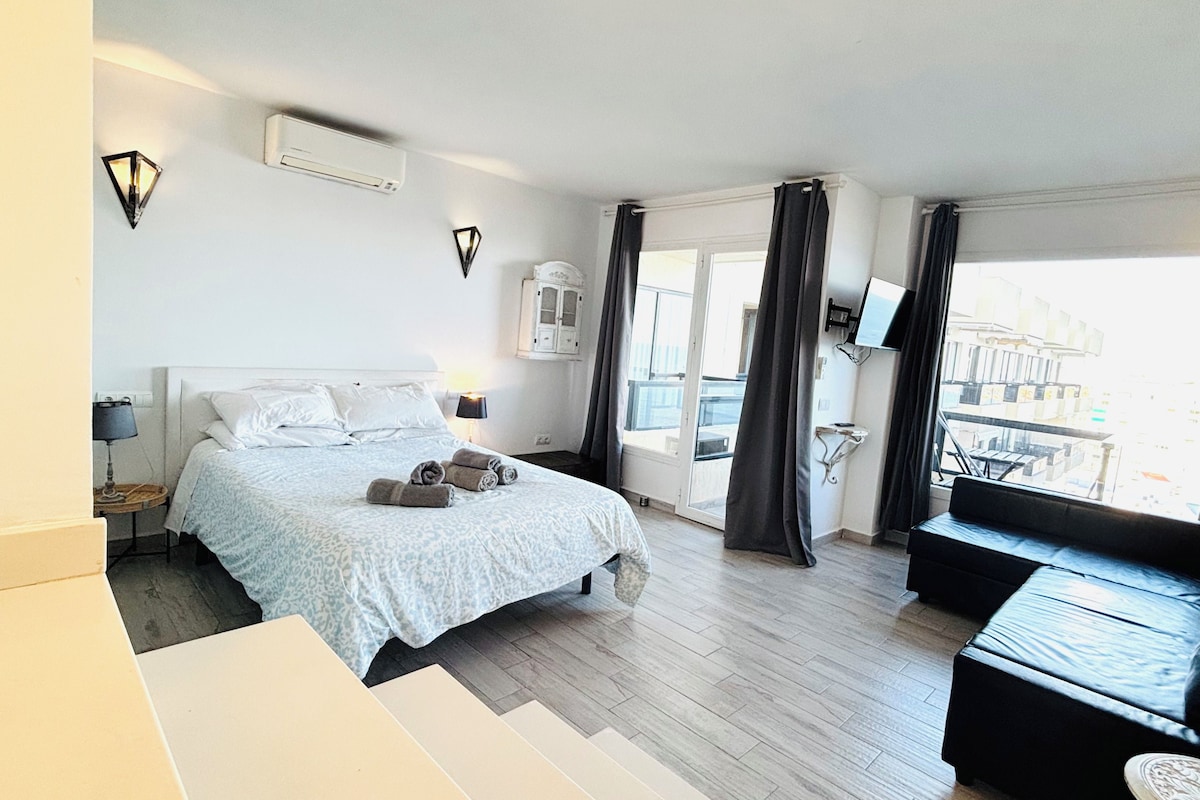 A hotel room with a bed, a sofa, a TV, and a balcony with curtains.