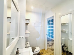 A bathroom with a toilet, sink, and mirror. There is a shower area with a glass door and a wooden floor. - Benalmádena Mood Aloha Beachfront (Benalmádena)