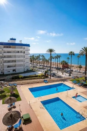 A hotel with a pool area, palm trees, and a view of the beach. - Benalmádena Mood Aloha Beachfront (Benalmádena)