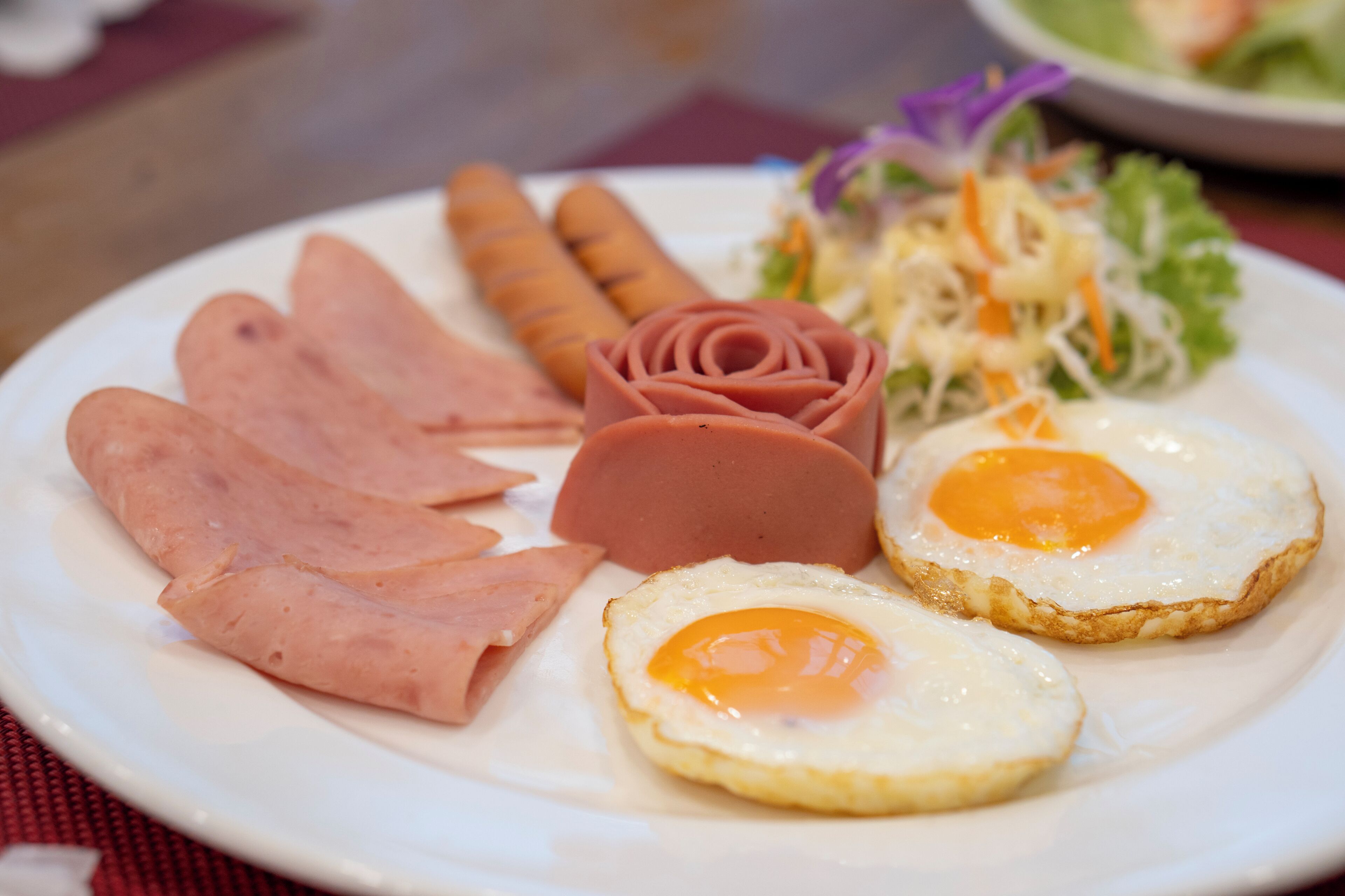 A plate with sliced ham, a sausage, two fried eggs, and a side salad.