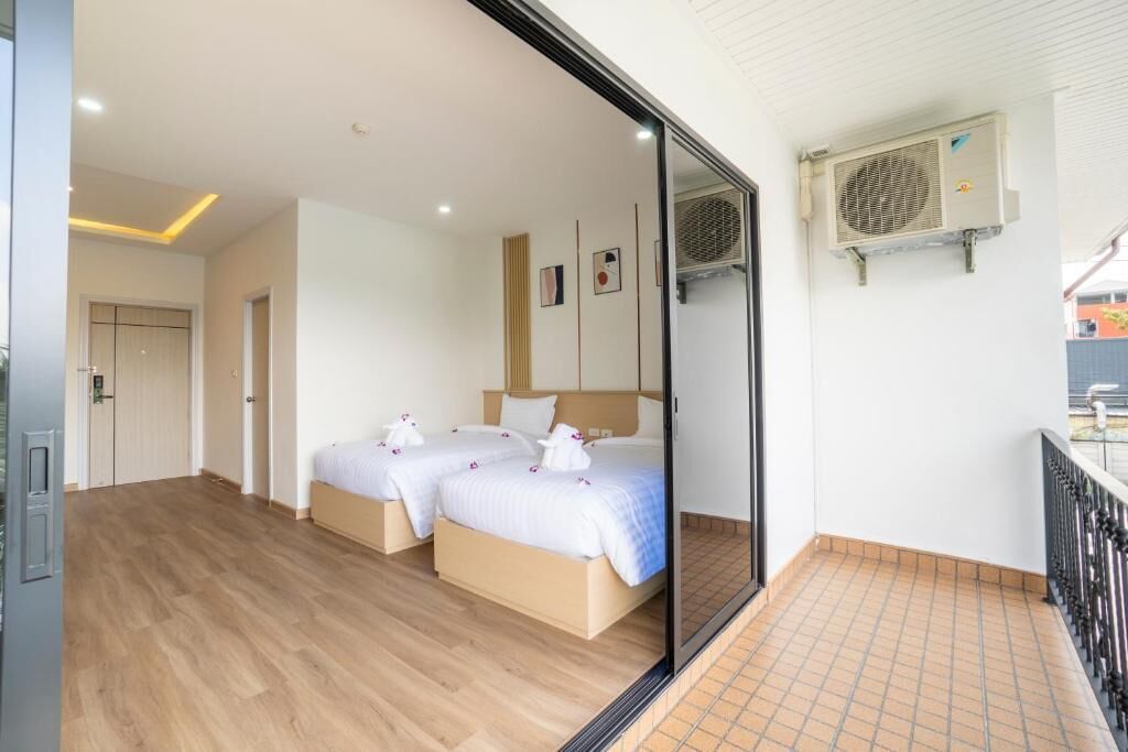A hotel room with two beds, a sliding door, an air conditioning unit, and a balcony with a railing.