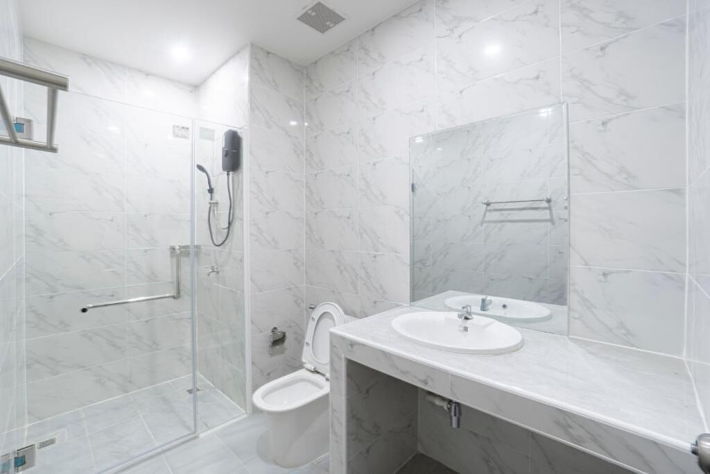 A bathroom with a glass shower enclosure, a toilet, a sink, and a mirror.