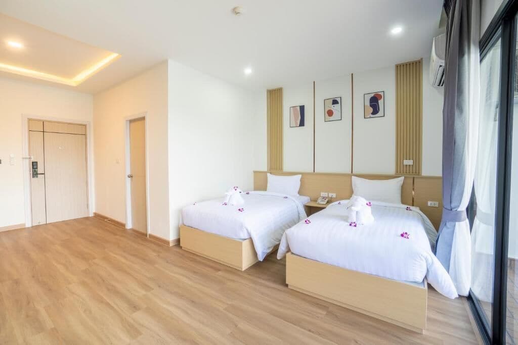 Habitación de hotel con dos camas, un ventanal grande y una puerta que da a un pasillo.