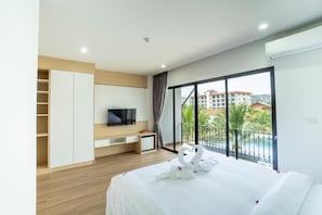 A hotel room with a bed, a TV, a wardrobe, and a balcony with a view of buildings and greenery. - PP Garden Home (Bangkok)