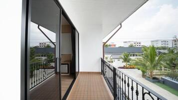 A balcony with a tiled floor, a black railing, and a view of buildings and palm trees.