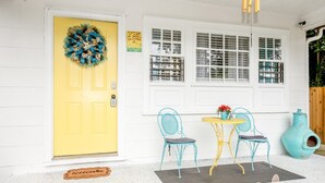 A yellow door with a wreath, a white window with shutters, and a blue chair outside. - Mercedes - Cozy Atlanta Bungalow Near Mercedes-Benz Stadium & Downtown (Atlanta)