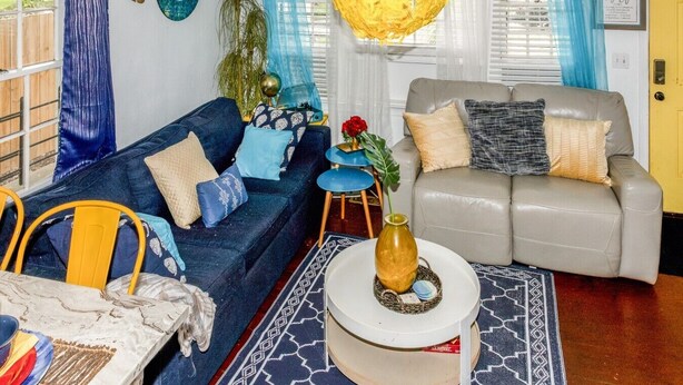 A living room with a blue sofa, a grey sofa, a round coffee table, and a yellow hanging light fixture. - Mercedes - Cozy Atlanta Bungalow Near Mercedes-Benz Stadium & Downtown (Atlanta)