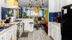 A compact kitchen with a central island, a dining area with a sofa and table, and a living room with a sofa and a coffee table. - Mercedes - Cozy Atlanta Bungalow Near Mercedes-Benz Stadium & Downtown (Atlanta)