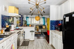 Eine kompakte Küche mit Kochinsel, ein Essbereich mit Sofa und Tisch sowie ein Wohnzimmer mit Sofa und Couchtisch.