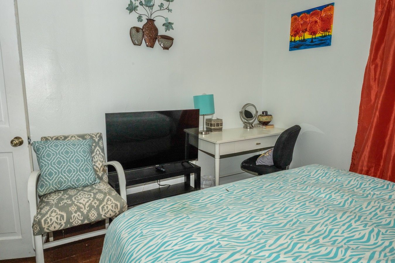 A bedroom with a bed, a desk with a television, a chair, and a wall decoration.