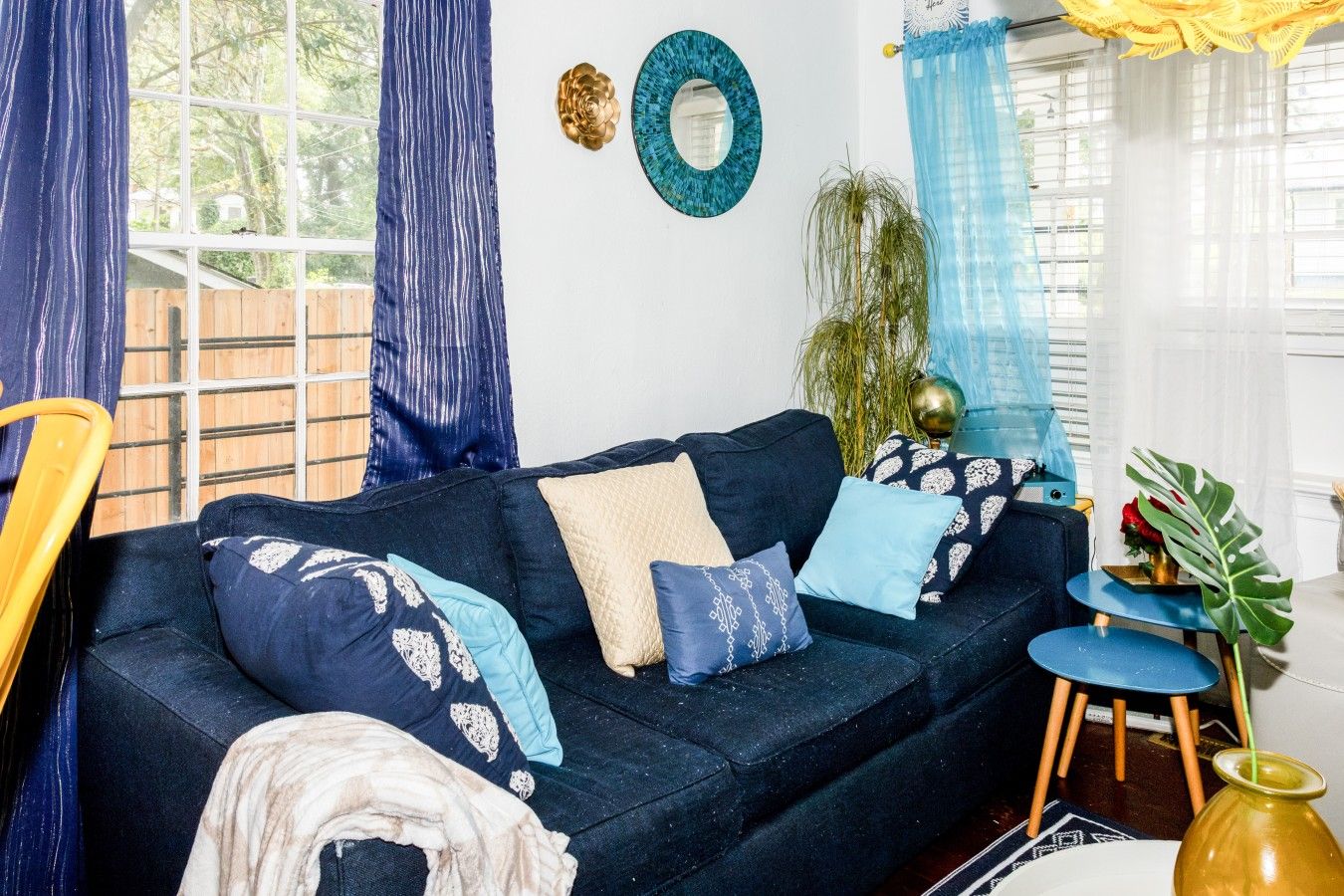 A living room with a dark blue sofa, patterned cushions, a small round table, and a potted plant.