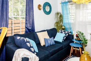 A living room with a dark blue sofa, patterned cushions, a small round table, and a potted plant. - Mercedes - Cozy Atlanta Bungalow Near Mercedes-Benz Stadium & Downtown (Atlanta)