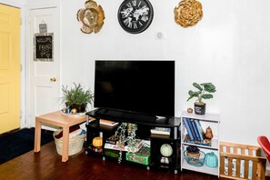 Ein Wohnzimmer mit Fernseher, einem Holznachttisch, einem Bücherregal und Wanddekorationen.