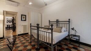 A bedroom with a metal bed frame, a bedside table, a nightstand, a radiator, a potted plant, and a door leading to another room. - Casa Dolce Roma – Your home in the heart of Rome! (Roma)