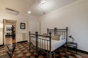 Ein Schlafzimmer mit einem Metallbettgestell, einem Nachttisch, einem Heizkörper, einer Zimmerpflanze und einer Tür zu einem anderen Raum.