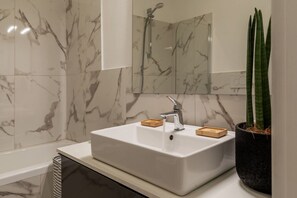 Un baño con lavamanos blanco, ducha de mano, espejo y planta en maceta.