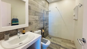 Un baño moderno con un lavamanos blanco, un espejo, un inodoro y una ducha con mampara de vidrio.