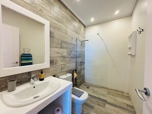 Casa de banho moderna com lavatório branco, espelho, sanita e cabine de duche com parede de vidro.