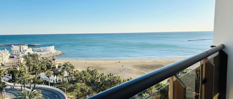 A balcony with a view of a beach, palm trees, and a road with a roundabout.