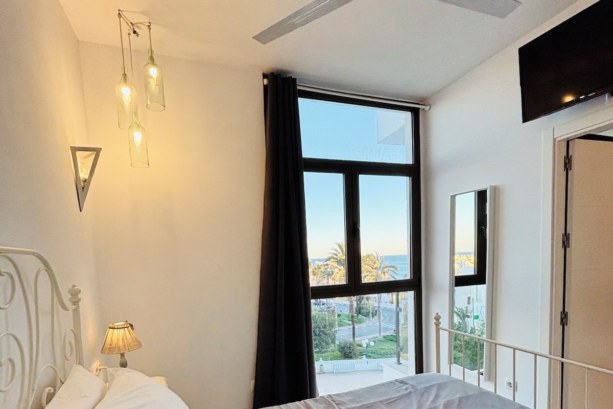 Quarto com cama, ventilador de teto, janela com vista e televisão fixada na parede.