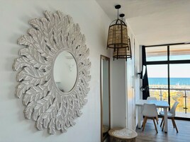 Ein Zimmer mit einem großen, verzierten Spiegel, einem Esstisch mit Stühlen und Meerblick durch große Fenster.