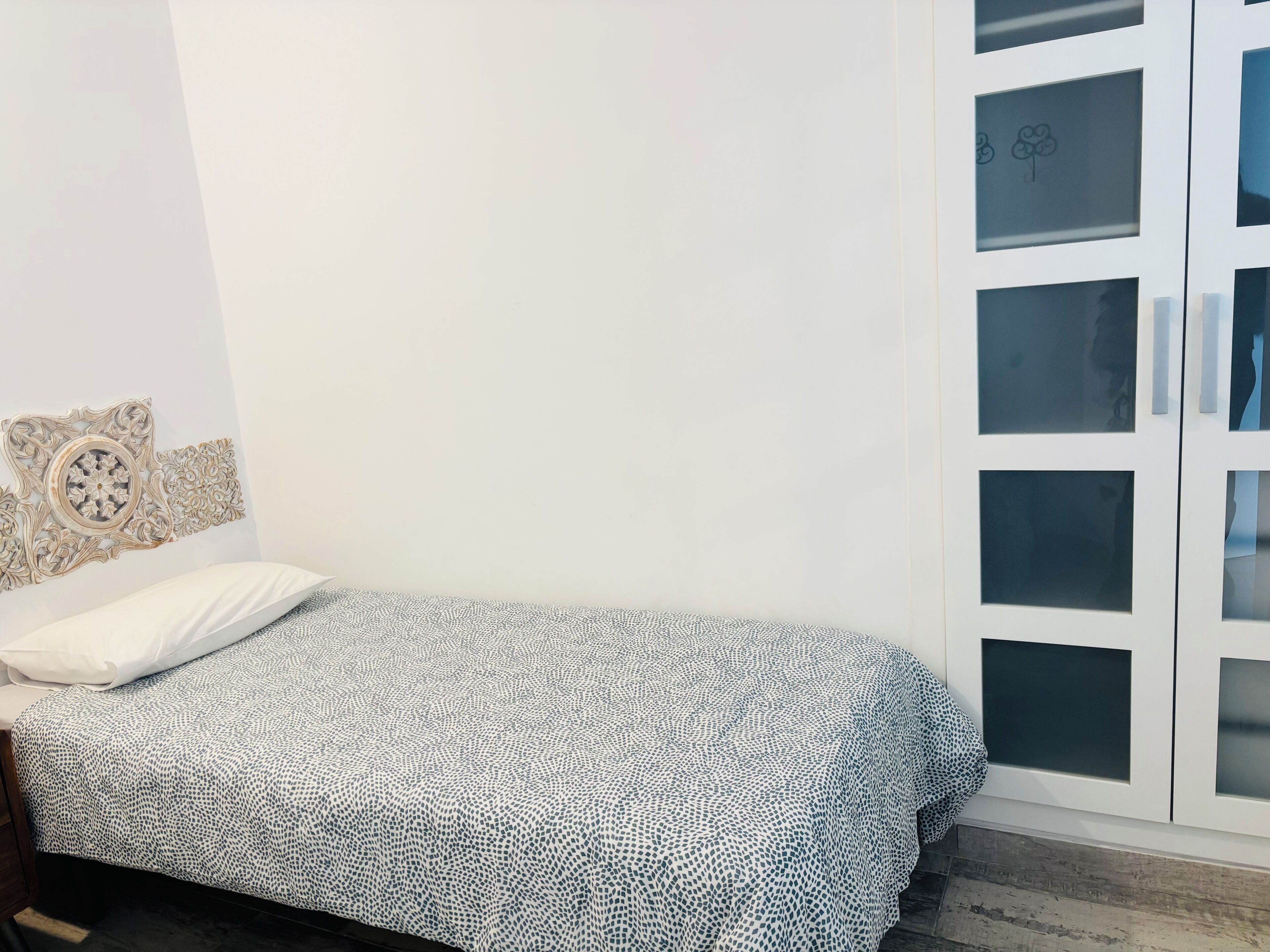 Quarto com uma cama, guarda-roupa com portas de vidro jateado e um objeto decorativo na parede.