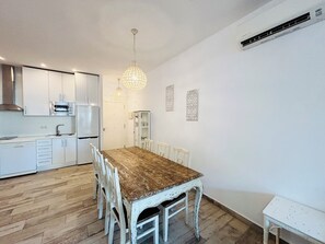 A modern kitchen with white cabinetry, a wooden dining table, and a hanging light fixture. - Benalmádena Mood Torremar Beach & Marina (Benalmádena)