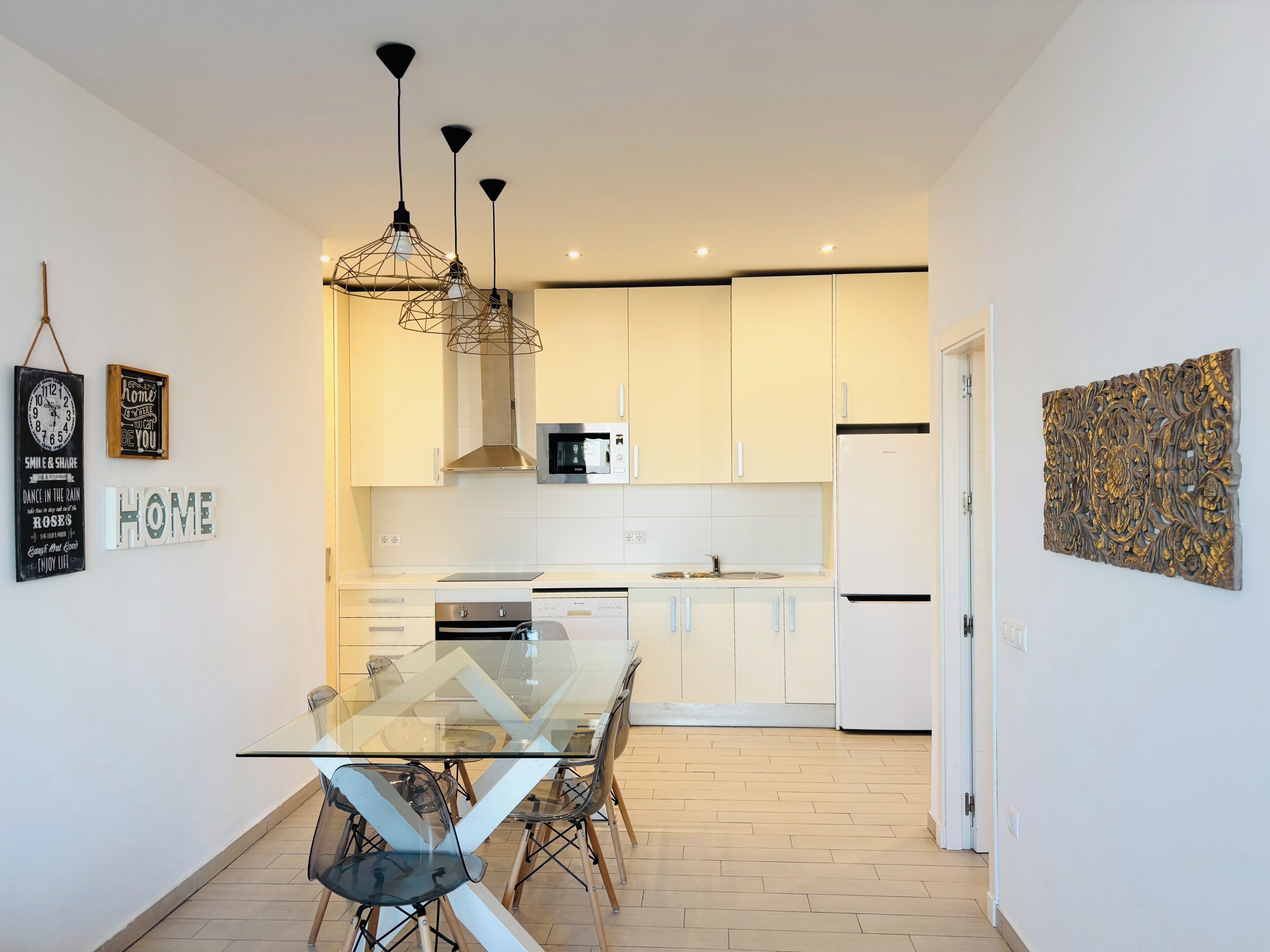 A modern kitchen with white cabinets, a glass dining table, and pendant lighting.