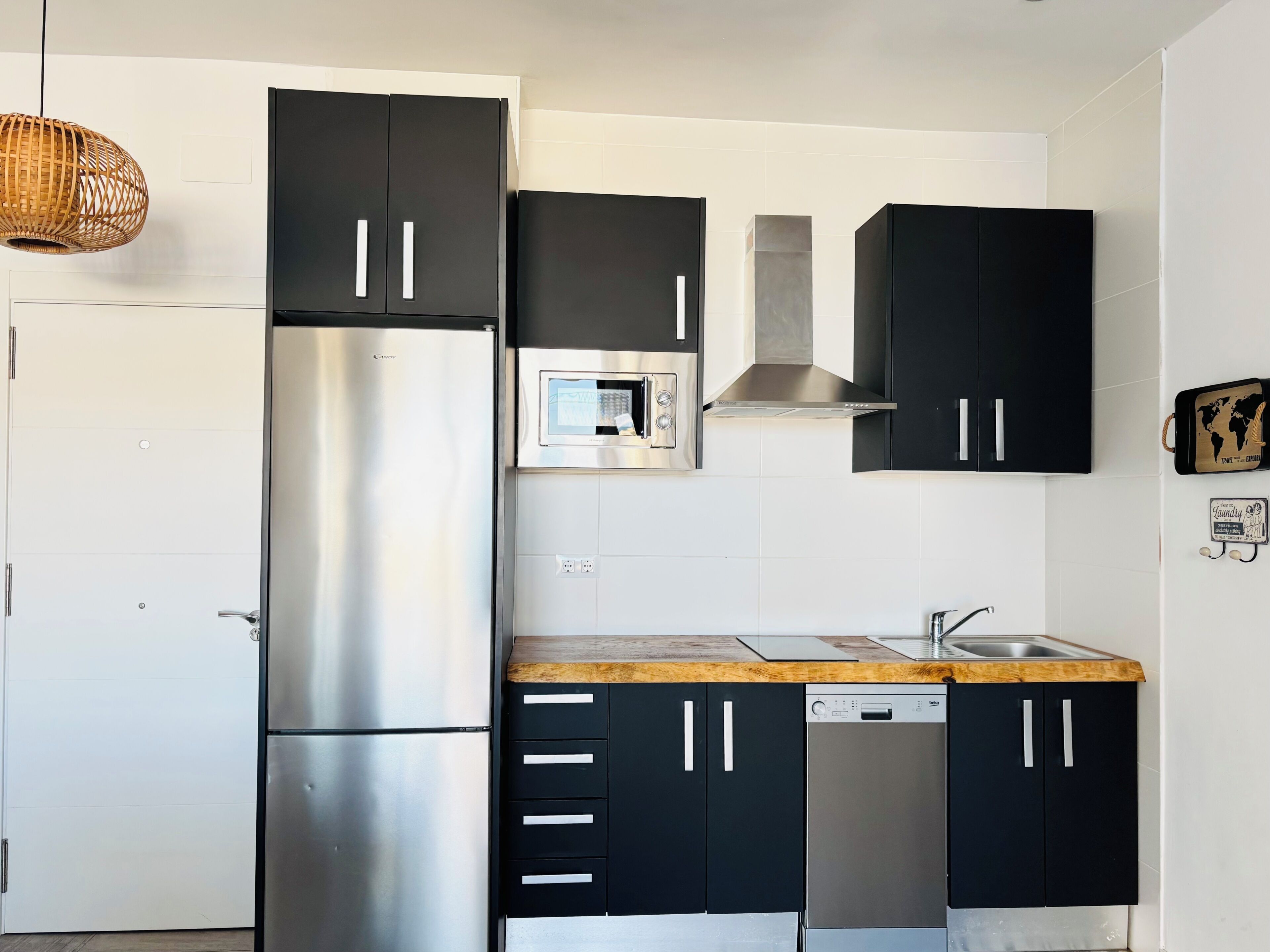 A modern kitchen with black cabinets, stainless steel appliances, and a wooden countertop.