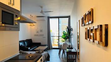 A modern kitchen with a microwave, stove, and ceiling fan. There is a dining area with a table and chairs, and a living space with a sofa.
