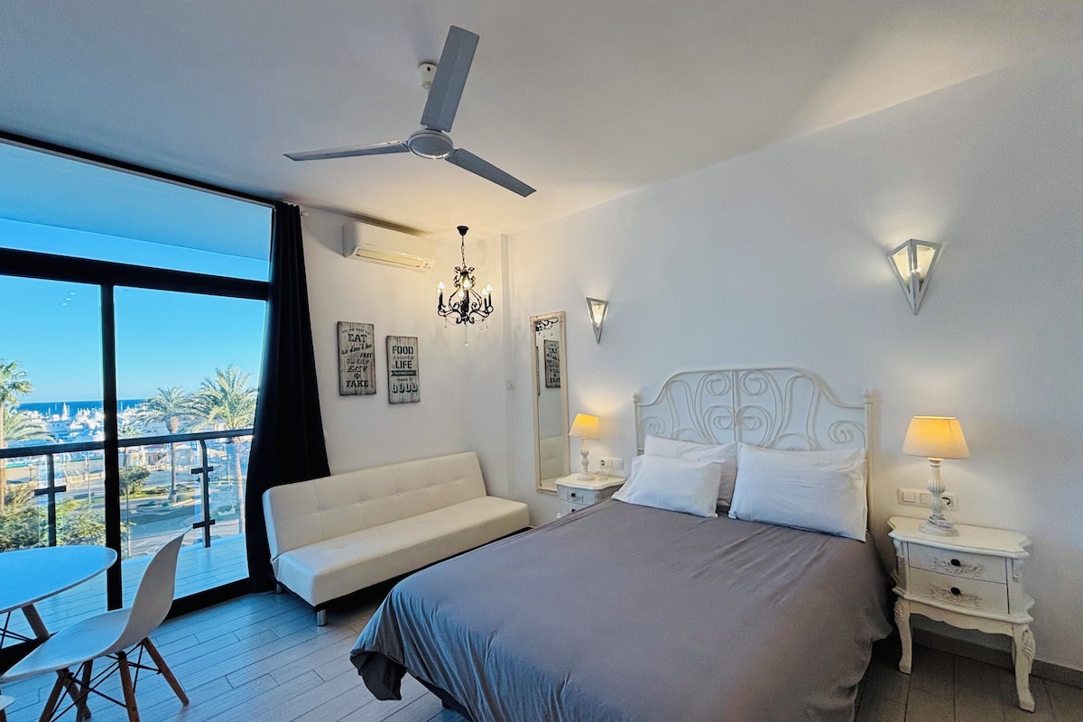 Quarto de hotel com cama, sofá, mesa de jantar e vista para o mar.