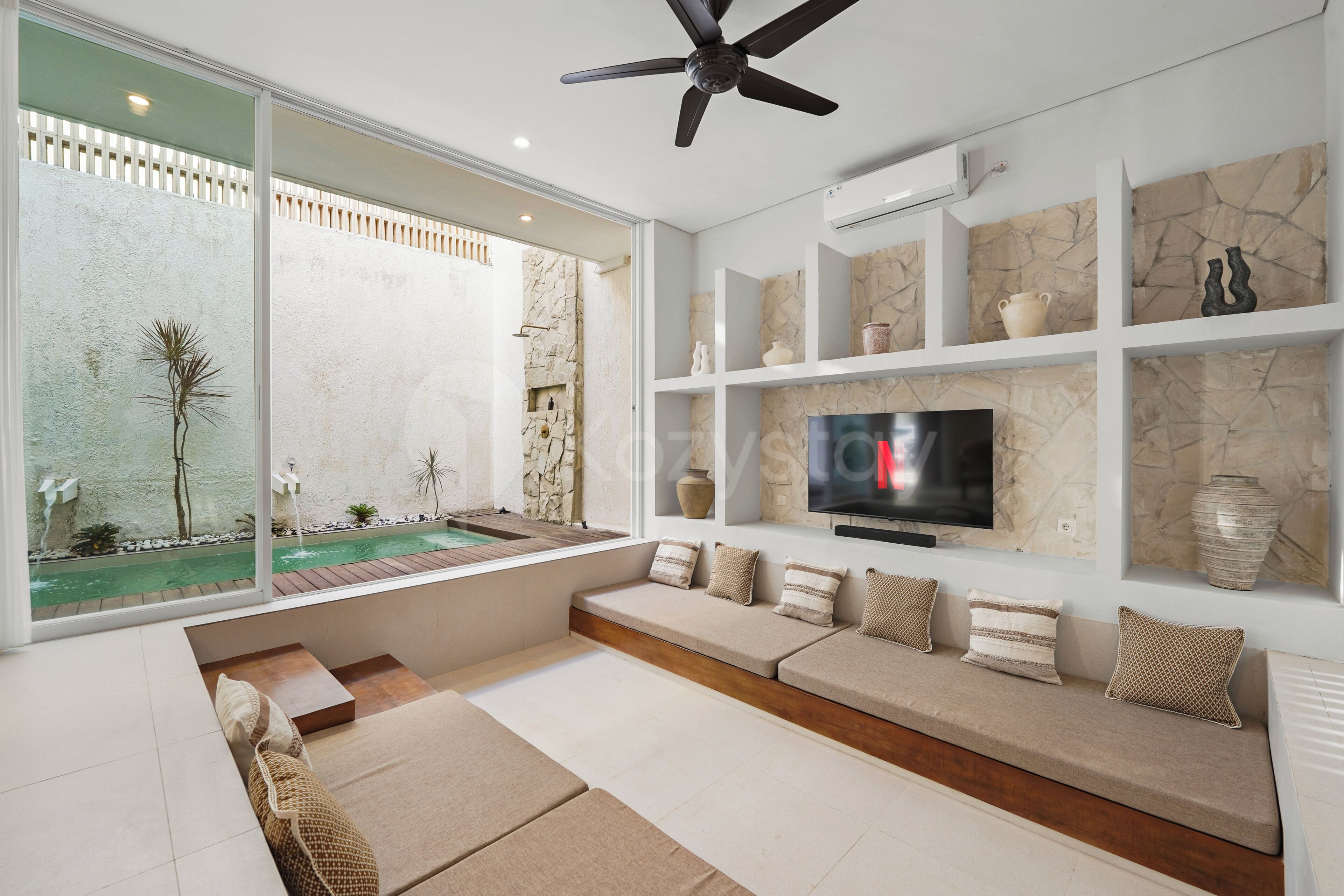 Una sala de estar moderna con una televisión grande, un ventilador de techo y vista a una piscina.