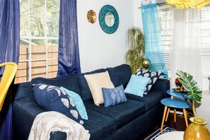 A living room with a dark blue sofa, patterned cushions, a round mirror, and a small side table with a globe and plant. - Cozy Bungalow near Downtown ATL (Atlanta)