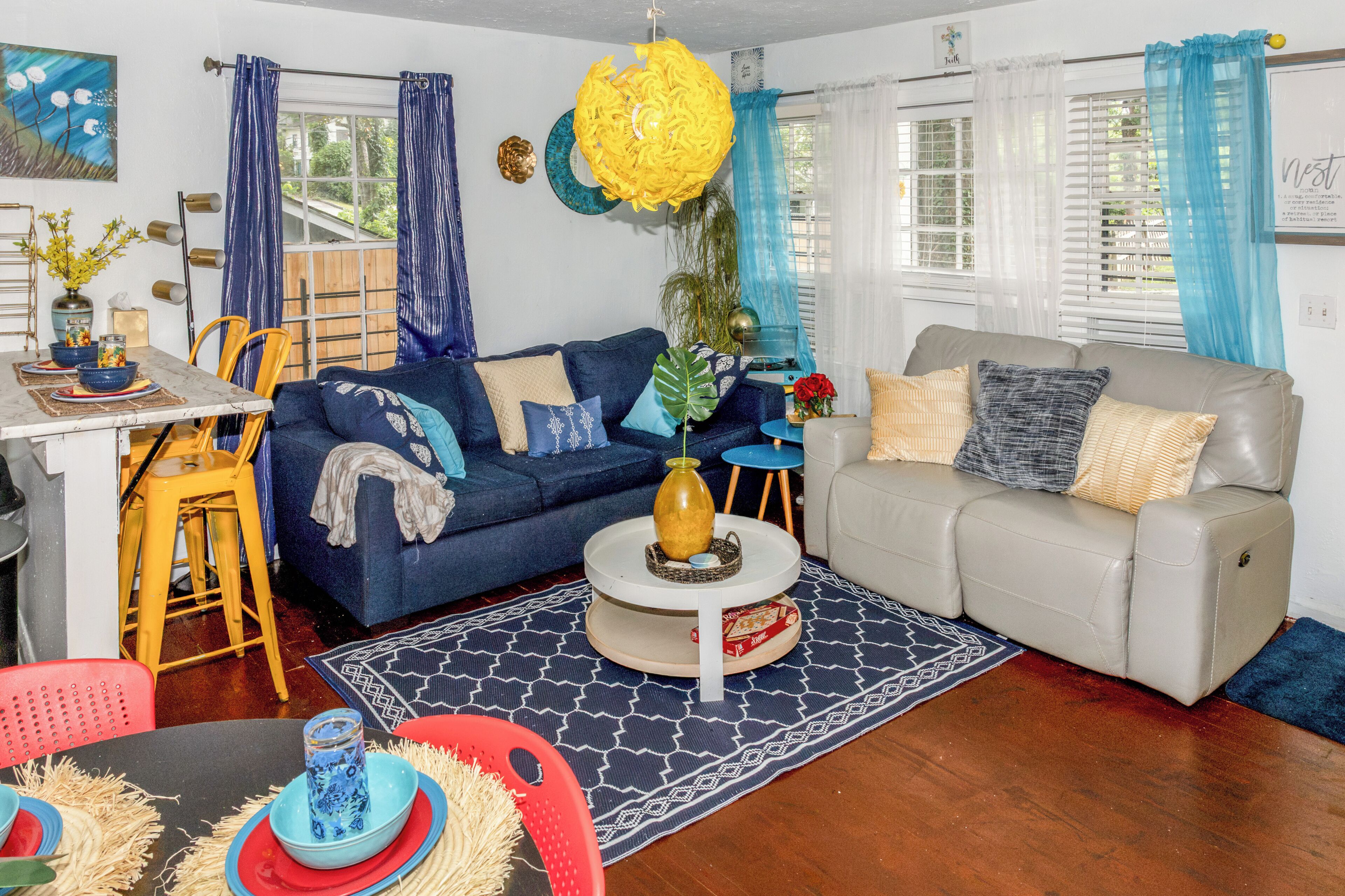 A living room with a blue sofa, a grey sofa, a coffee table, and a dining area with chairs and a table.