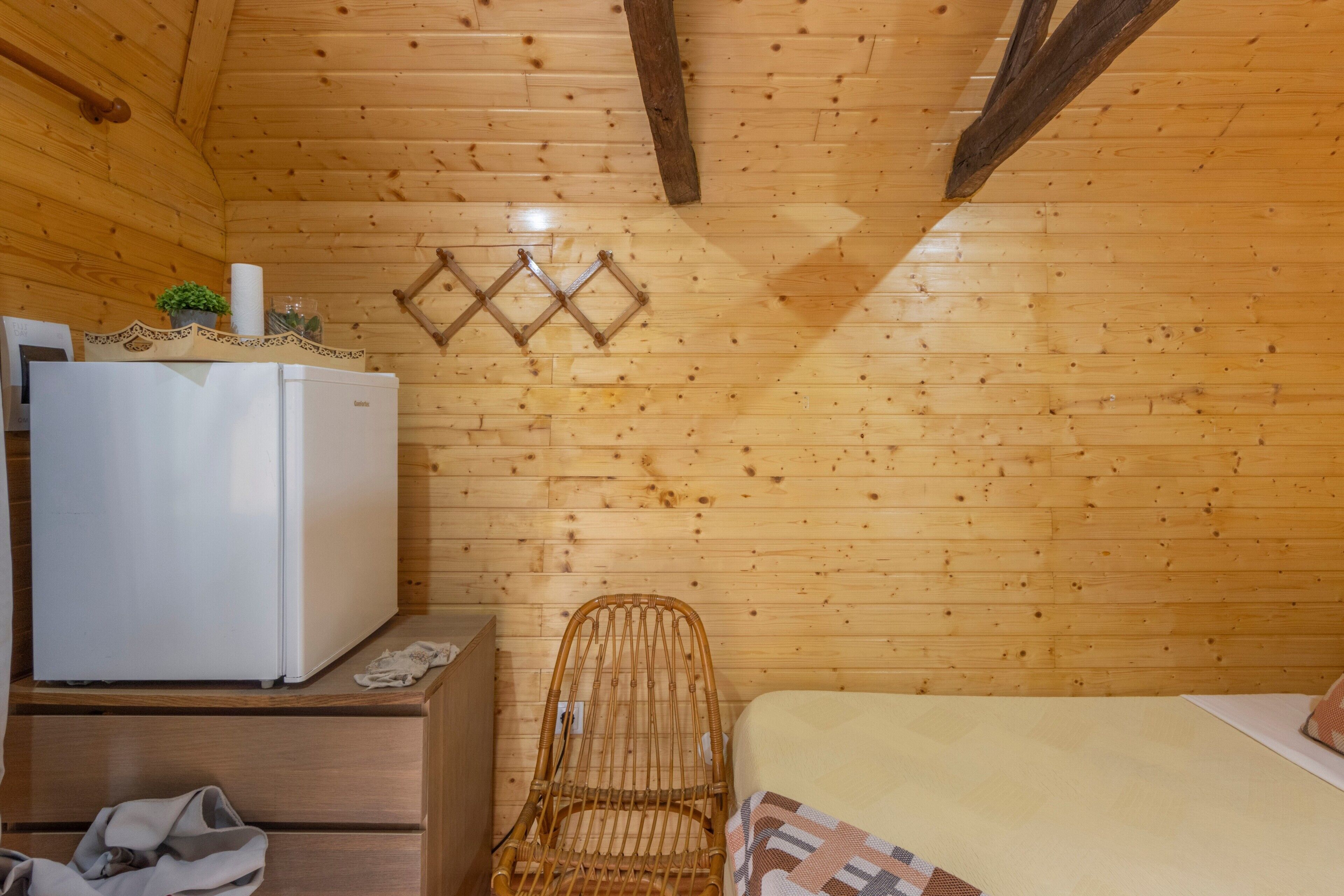 A wooden cabin room with a bed, a chair, a dresser, and a refrigerator.