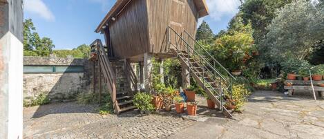 A wooden structure with a staircase leading to a platform, surrounded by potted plants and a cobblestone ground.