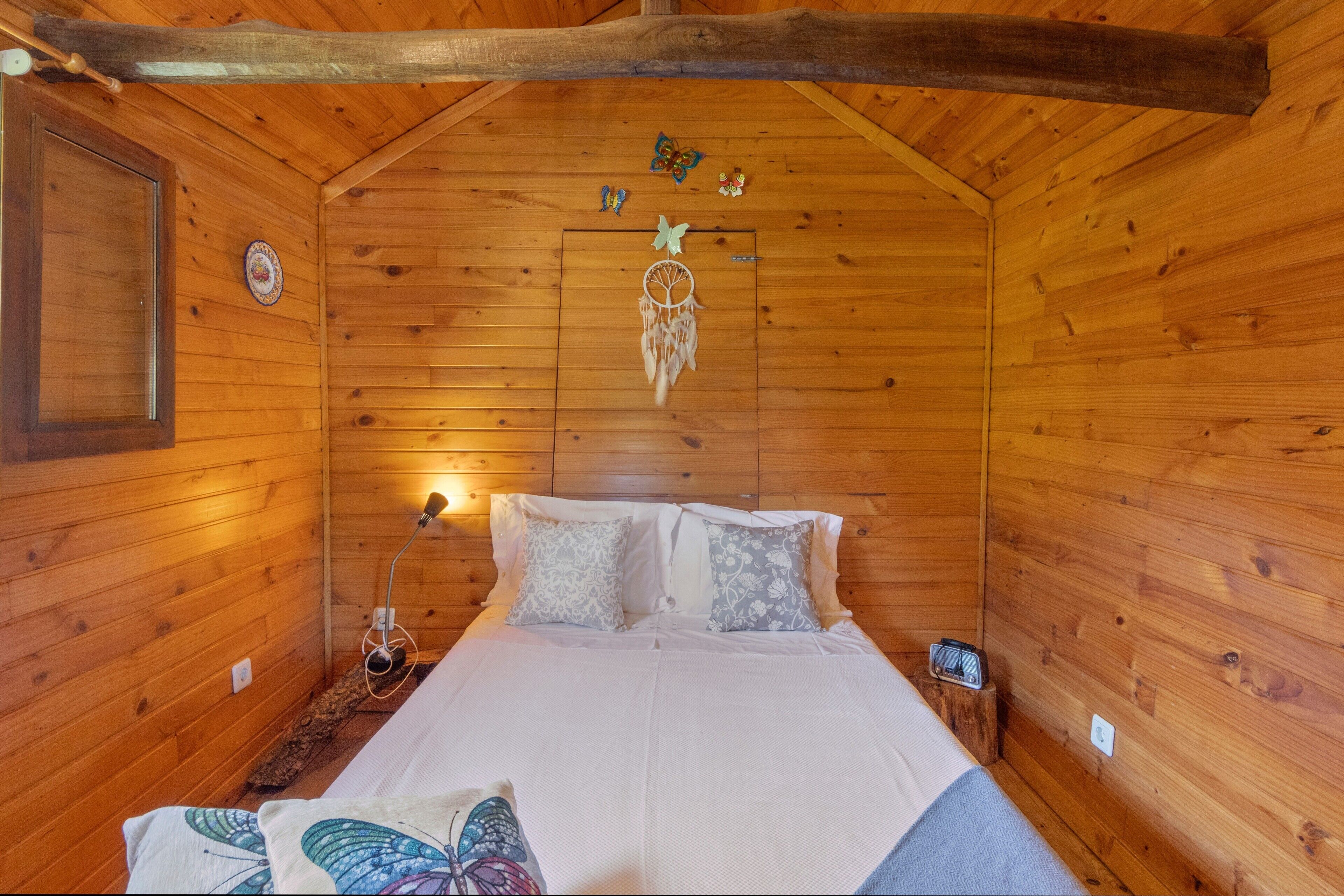 Une chambre dans une cabane en bois, avec un lit, des oreillers, un attrape-rêves et une lampe.