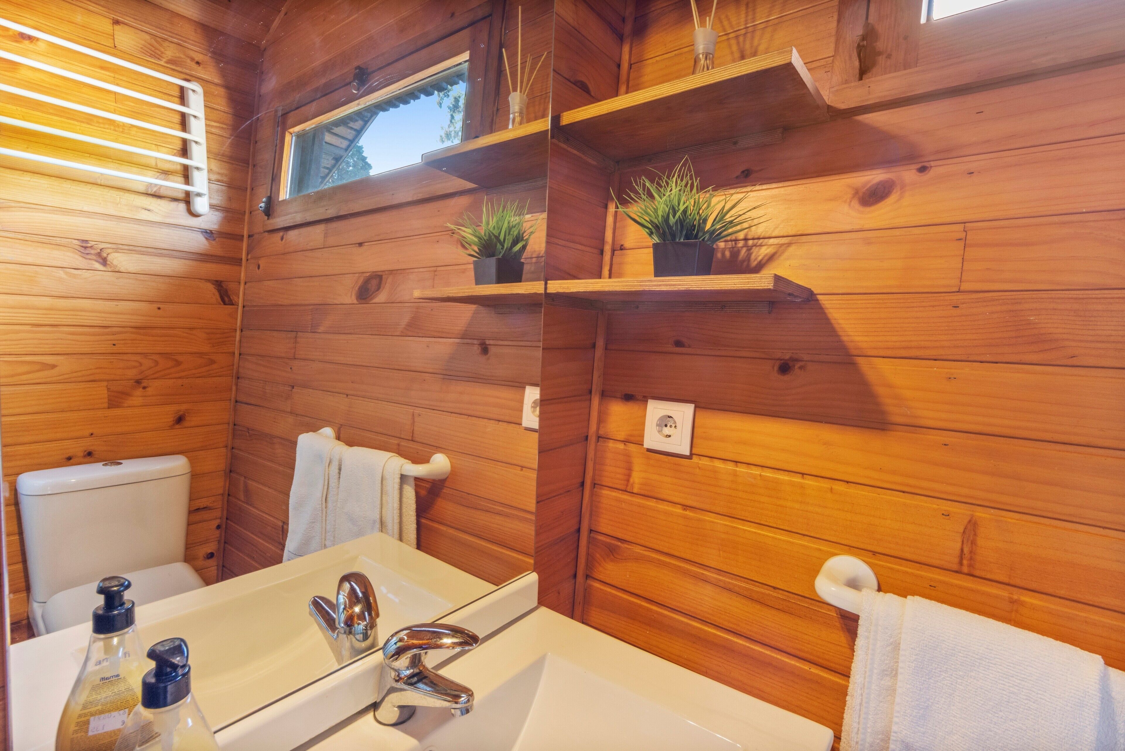 A wooden cabin bathroom with a white sink, chrome faucet, and two small potted plants on shelves.