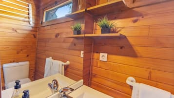 A wooden cabin bathroom with a white sink, chrome faucet, and two small potted plants on shelves.